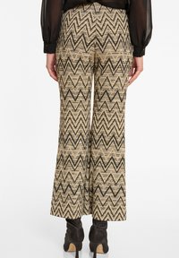 Pantalons taille haute évasés en beige avec un motif zigzag noir, dotés d'un tissu texturé et d'une finition soignée à l'ourlet.
