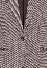 Gros plan d'un blazer rayé diagonal gris et blanc avec un seul bouton foncé et deux poches passepoilées à l'avant.