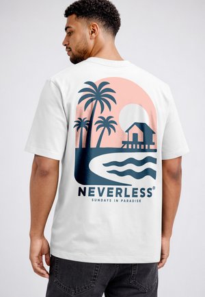 Man wearing white T-shirt with a sunset beach scene, palm trees, a hut, water waves, and the text "NEVERLESS SUNDAYS IN PARADISE" on the back.