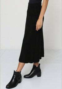 Jupe midi noire avec un motif texturé, associée à des bottines noires à talon carré et avec un détail de fermeture éclair sur le côté.