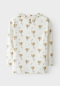 Maglietta a maniche lunghe color crema con un motivo floreale che presenta fiori marrone chiaro e fate, rifinita con un colletto arricciato e una chiusura con bottone di legno.