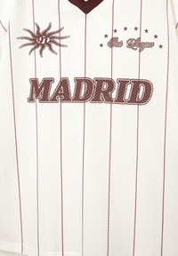 Weißes Sporttrikot mit kastanienbraunen vertikalen Streifen, „MADRID“-Schriftzug, Sonnenmotiv und „Unsere Liga“-Schriftzug über Sternen. Hergestellt aus atmungsaktivem Material.
