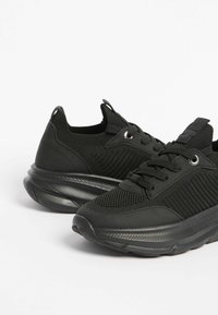 Melnas sporta kurpes ar teksturētu adījuma augšdaļu, polsterētu mēleni un izturīgu gumijas zolīti ar viļņotu dizainu. Iekļautas auklas un metāla acu stiprinājumi.