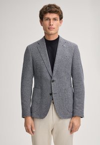 Blazer in misto lana grigio con motivo a quadri, chiusura a un bottone, rever a notched, e due tasche, abbinato a un dolcevita nero.