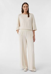 Cremiger Strickpullover mit rundem Ausschnitt und 3/4-Ärmeln, kombiniert mit weit geschnittenen, cremfarbenen Hosen mit elastischem Bund und Seitentaschen.
