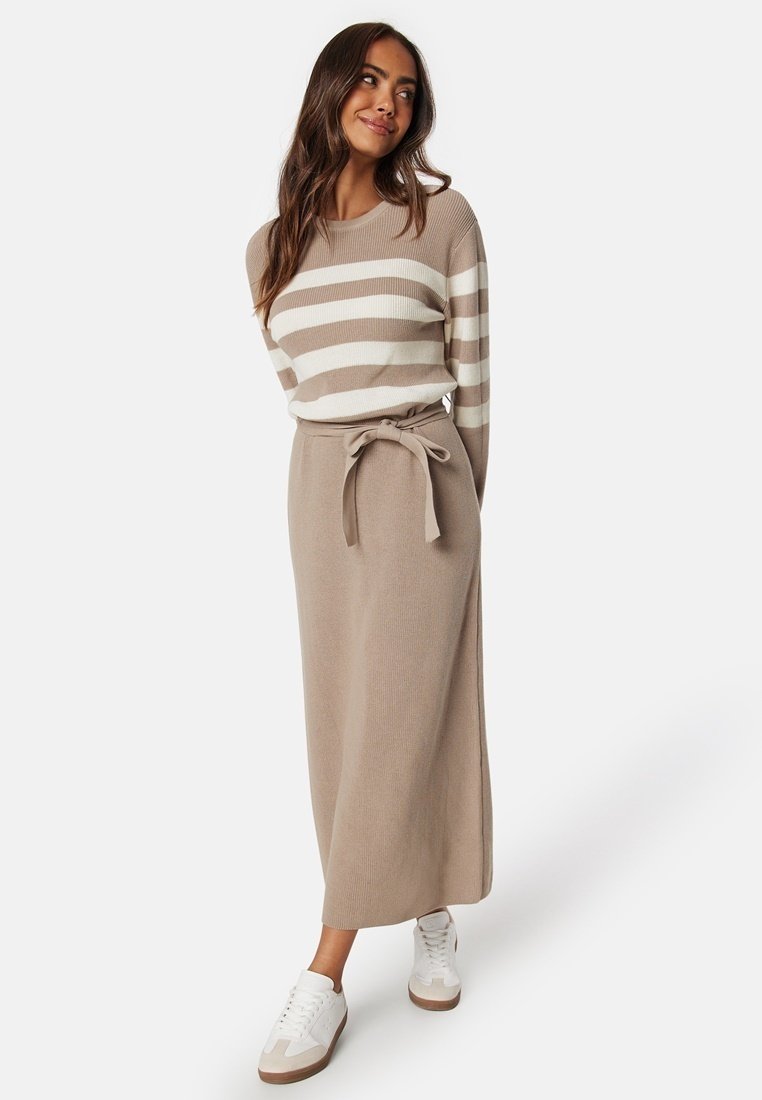 Pullover lavorato a maglia a righe in avorio e beige abbinato a una gonna lunga beige con cintura in vita e sneakers bianche.
