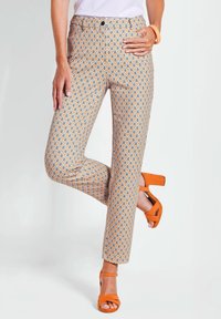 Pantaloni a fantasia con un motivo a rombi nei colori arancione, blu e crema, con una vestibilità aderente e chiusura con bottone. Indossati con tacchi arancioni.