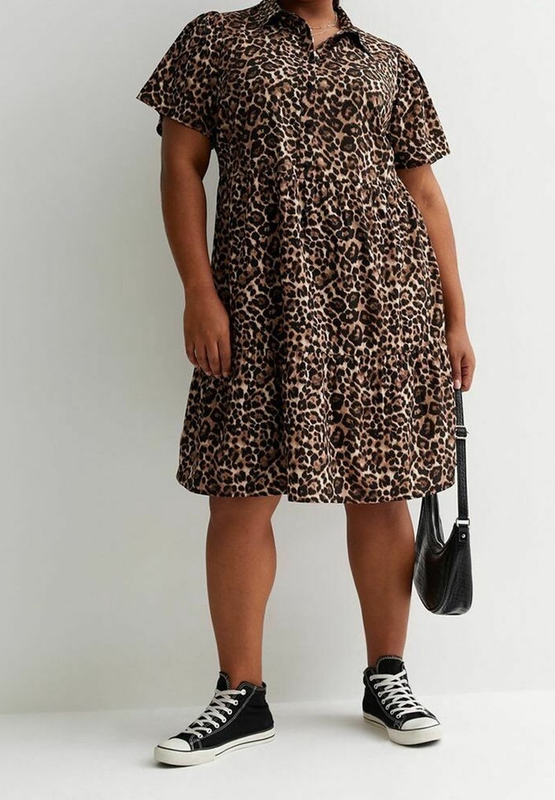 Abito in stampa leopardata con colletto, maniche corte e gonna a strati; abbinato a sneakers nere alte e una piccola borsa nera.