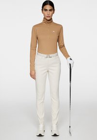 Strój golfowy z jasnobrązową, wzorzystą bluzką z długim rękawem oraz białymi, dopasowanymi spodniami. Dodatki to srebrny pasek i kij golfowy.