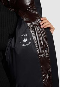 Black coat with shiny brown inner lining, featuring a white logo with a leaf. Includes a zippered pocket and snap button details.