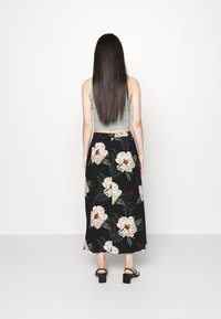 Falda maxi floral en negro con grandes peonías crema y hojas verdes; combinada con un top corto de tono verde claro y sandalias negras de tacón bloque.