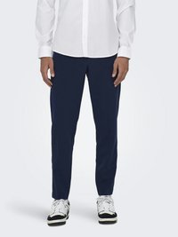 Marinblå skräddarsydda byxor i lätt tyg, kombinerade med en vit skjorta med knappar och svart-vita sneakers.