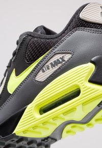 Černá teniska se žlutými akcenty, která má strukturovaný svršek, viditelnou vzduchovou polstrování v podrážce a šedý detail "AIR MAX" na boku.