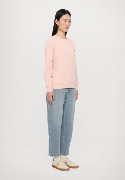 Lyserød sweatshirt med lange ærmer, ribbede manchetter og et lille logo. Matchende med løse lyseblå jeans og beige sneakers.