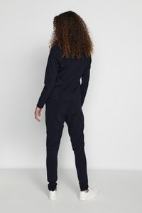 Navy blue tracksuit featuring a fitted top and tapered pants, made of smooth fabric with elastic cuffs and waistband. White sneakers complete the look.