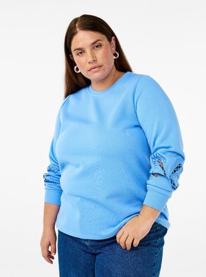 Hellblaues Sweatshirt mit Rundhalsausschnitt und texturierten Spitze-Details an den Ärmeln. Weicher Stoff mit lockerer Passform. Kombiniert mit Jeans.