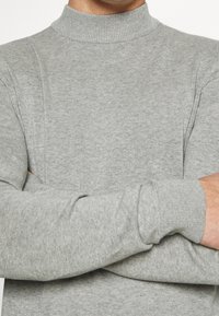 Pull en col roulé gris fabriqué en matériau tricot doux. Possède des poignets et un col côtelés, une texture lisse et une coupe ajustée avec des coutures minimales.