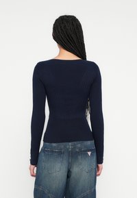 Tmavomodrý rebrovaný top s dlhými rukávmi, ktorý je v páse priliehavý a má široký výstrih. Má textúrované panely a gombíky na rukávoch.