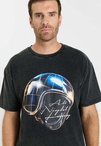 Zwart katoenen T-shirt met een grafische print van een helm met een rasterpatroon, geaccentueerd met blauwe en witte accenten en de tekst "All Night Long."