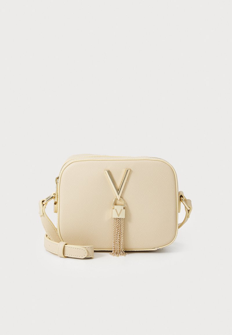 Beige crossbody bag made of textured material. Features a prominent "V" logo, tassel accent, and gold hardware. Adjustable strap included.