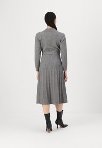 Abito grigio lavorato a maglia con corpetto aderente e gonna plissettata, dotato di maniche lunghe e di un nastro di tessuto in vita. Stivaletti neri con tacco.