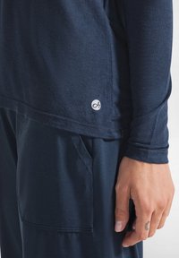 Camicia a maniche lunghe blu navy con un tessuto texturizzato, caratterizzata da un logo sottile vicino all'orlo. Il tessuto sembra morbido e leggero.