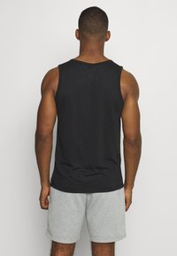 Czarny bezrękawnik wykonany z bawełny, z okrągłym dekoltem i luźnym krojem. W zestawie z szarymi bawełnianymi szortami. Widok z tyłu.