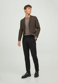 Blazer checkered marrone sopra un maglione grigio, abbinato a pantaloni neri e scarpe nere, con una texture liscia e una vestibilità su misura.