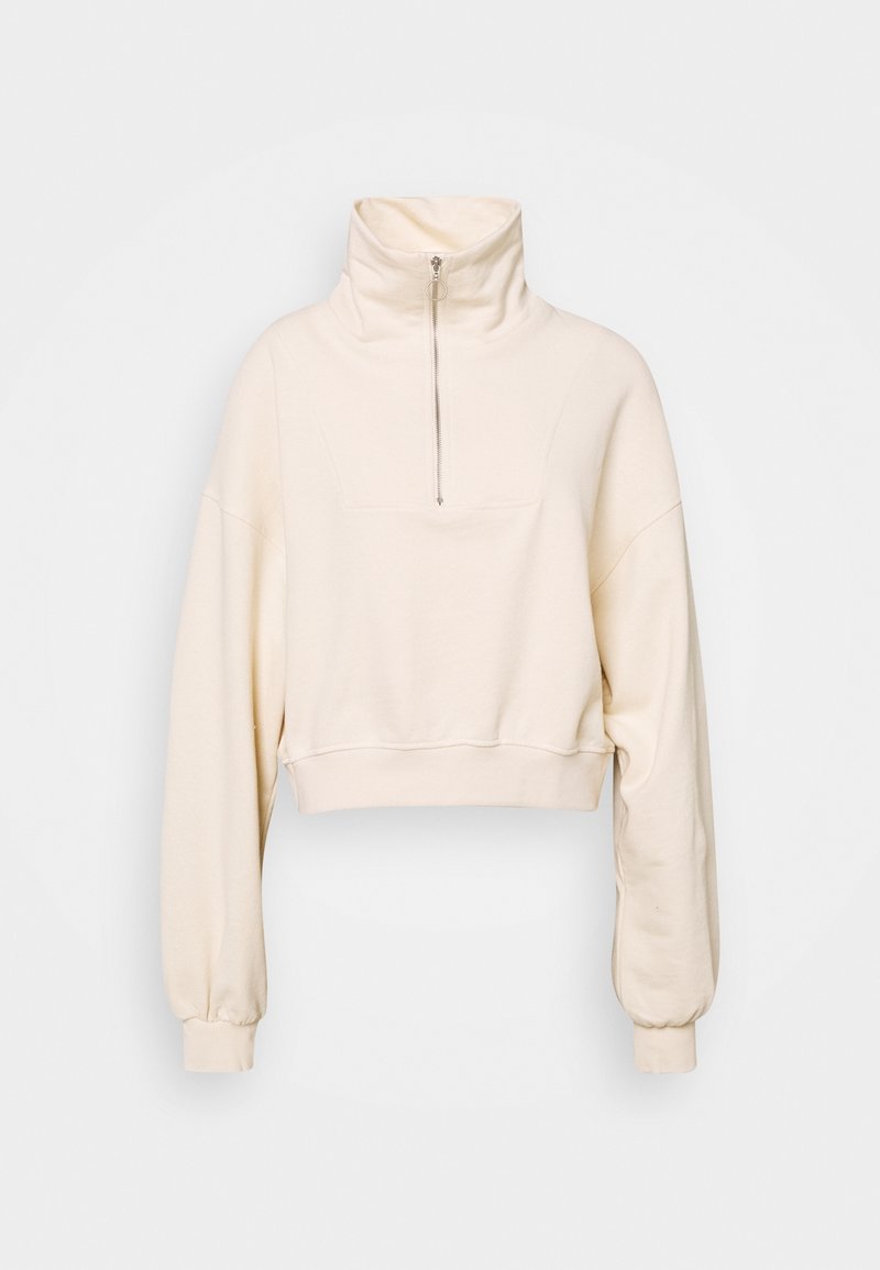 Sudadera recortada en color crema, con cuello alto, cierre de media cremallera y mangas voluminosas. Textura suave con un dobladillo ajustado.