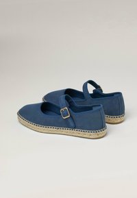 Espadrilles de lona azul con un detalle de correa y hebilla, que cuentan con una suela de yute natural. Punta redondeada y textura suave.