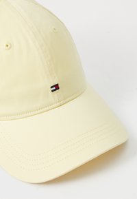 Casquette de baseball en coton jaune avec une visière courbée, présentant un petit logo brodé rouge, blanc et noir sur le panneau avant.