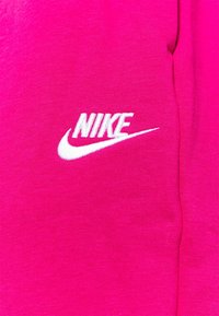 Fuchsiová tkanina Nike s bílým vyšívaným logem a hladkou texturou. Design zahrnuje grafiku swoosh pro branding.