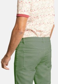 Camisa de manga corta con un patrón floral en suaves colores pastel; pantalones verdes de corte ajustado con bolsillos traseros, de textura suave.