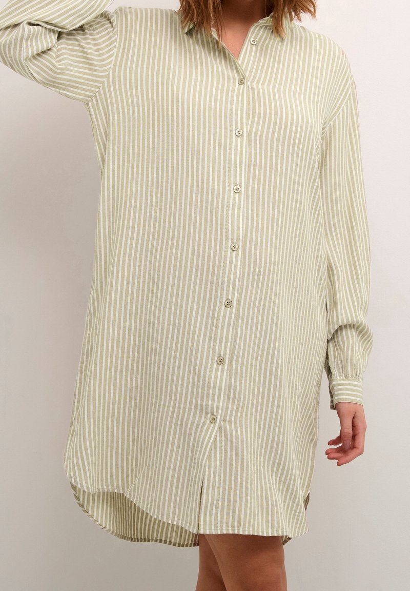 Robe chemise à manches longues à rayures verticales vert clair et blanc, portée par une personne aux cheveux mi-longs.