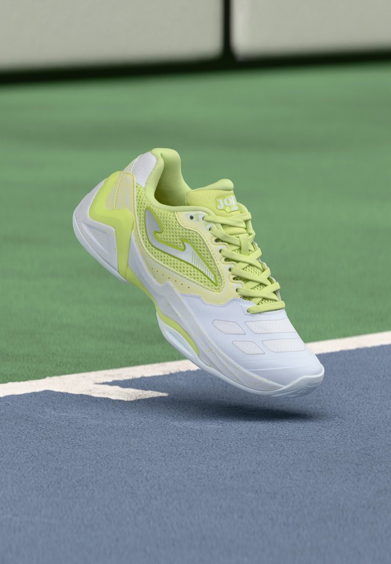 Αθλητικό παπούτσι ανοιχτού πράσινου και λευκού χρώματος με πλέγμα και συνθετικά πάνελ, που αιωρείται πάνω από την επ ιφάνεια γηπέδου τένις σε μπλε και πράσινο χρώμα.