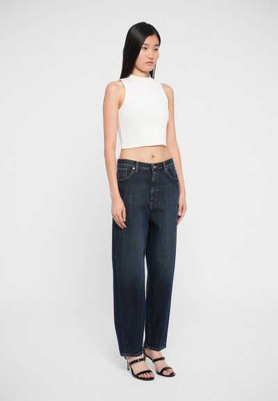 Bílý zkrácený halter top, tmavě modré volné džíny a černé sandály na vysokém podpatku. Hladká tkanina, vysoký pas a rovný střih nohavic.