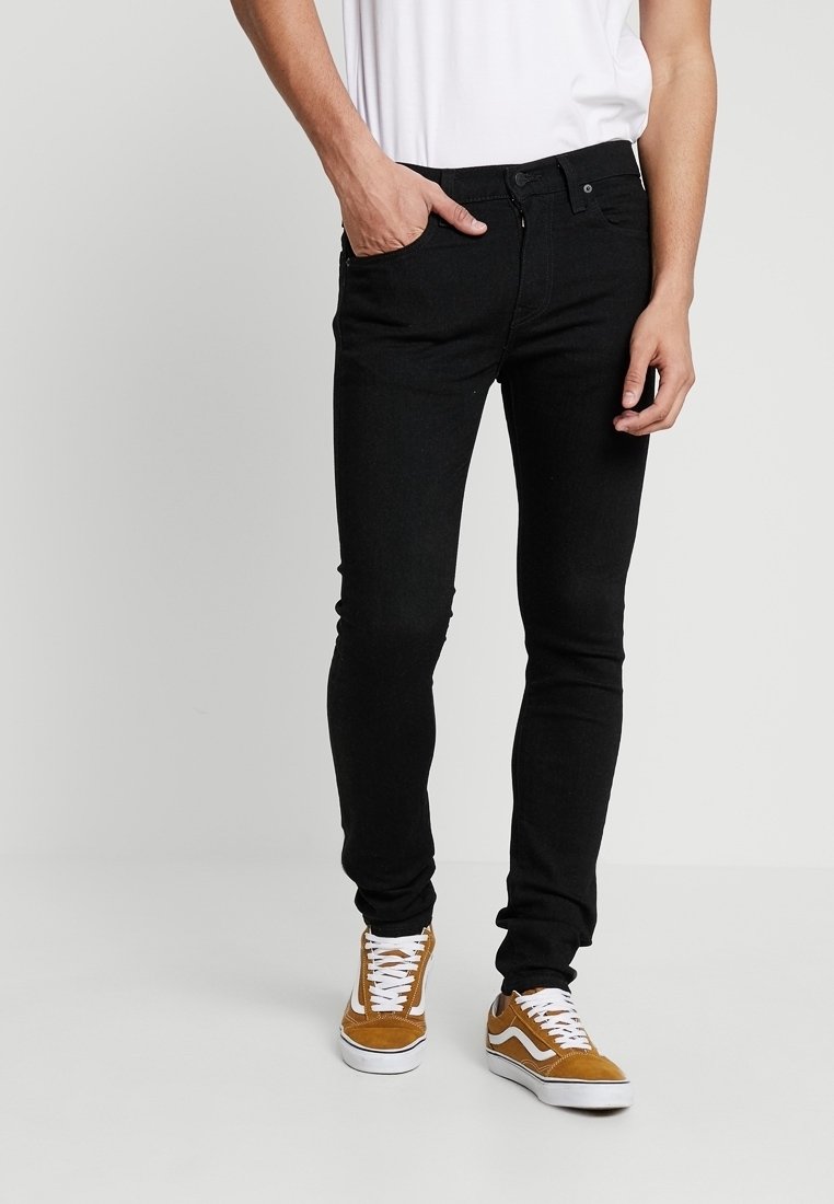 Jeans skinny negros con cierre de cremallera y botón, combinados con zapatillas blancas y una camiseta blanca sin estampado. Textura de denim suave.