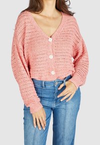 Rosa stickad cardigan med V-ringning, stor knappstängning och lösa, strukturerade ärmar. Matchas med högmidjade blå jeans.