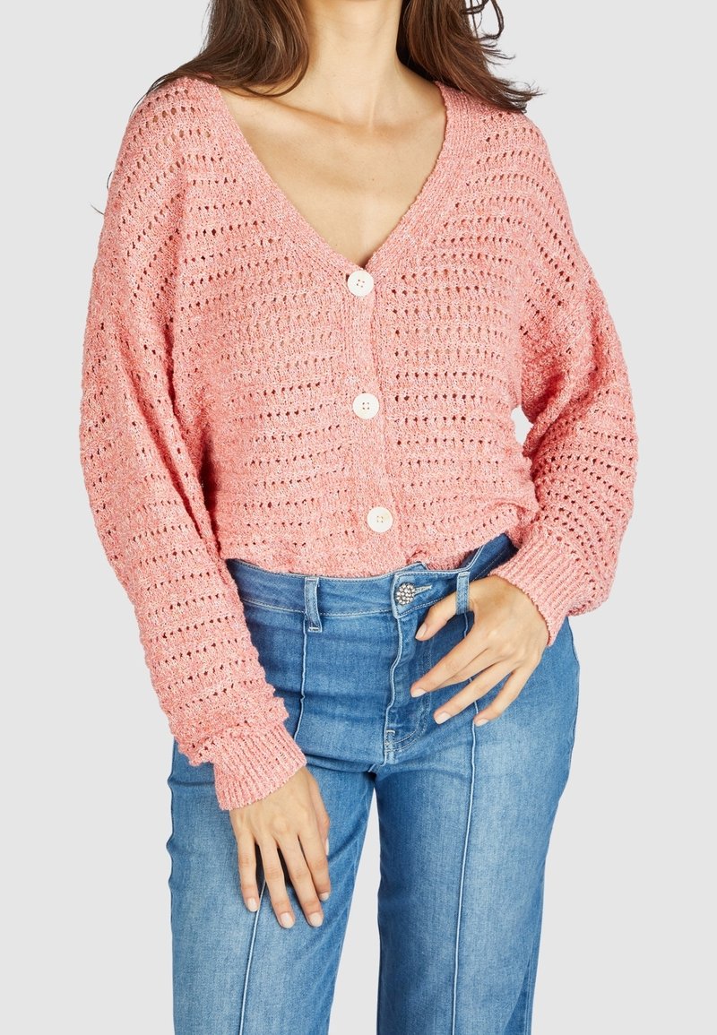 Rosa stickad cardigan med V-ringning, stor knappstängning och lösa, strukturerade ärmar. Matchas med högmidjade blå jeans.