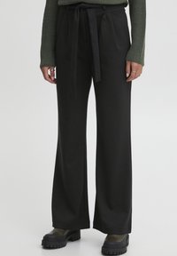 Pantalons larges noirs en tissu doux avec une ceinture �à nouer assortie. Présente des plis à l'avant, associés à des bottes noires robustes.