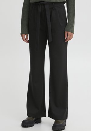 Pantalons larges noirs en tissu doux avec une ceinture à nouer assortie. Présente des plis à l'avant, associés à des bottes noires robustes.
