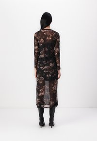 Robe noire transparente à manches longues, dotée d'un motif floral dans des tons de marron et d'une longueur mi-mollet. Portée avec des bottes noires hauteur genou.