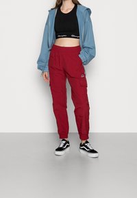 Jasnoniebieska bluza z kapturem na zamek błyskawiczny, czarny krótki top, czerwone spodnie cargo z bocznymi kieszeniami oraz czarno-białe tenisówki.