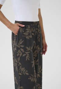 Black wide-leg pants featuring a gold leaf pattern, elastic waistband, and side pockets. The fabric has a light, soft texture.