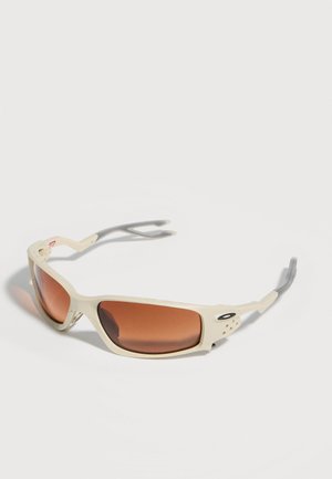 Beżowe sportowe okulary przeciwsłoneczne z brązowymi prostokątnymi szkłami i zakrzywionymi zausznikami, leżące na białej powierzchni.