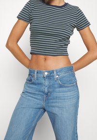 Randig kort topp i mörkgrön och marinblå, med rund halsringning. Kombinerad med ljusblå högmidjade jeans.