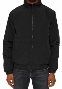 Giacca nera con zip, colletto alto, polsini elasticizzati e vestibilità cropped. Caratterizzata da un tessuto liscio e leggero e una tasca frontale.