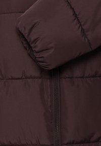 Gros plan d'un tissu matelassé brun foncé avec des lignes horizontales cousues et un détail de fermeture éclair centrale.