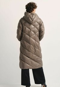 D ługi, puchowy płaszcz z kapturem w jasnym odcieniu taupe. Posiada pikowanie w kształcie diamentów, gładką fakturę i sięga do połowy łydki.