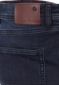 Granatowe dżinsy w denimie z brązową skórzaną naszywką z napisem "CASA MODA." Posiadają proste szwy i standardową tylnią kieszeń.